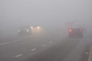 cars drive over through thick fog